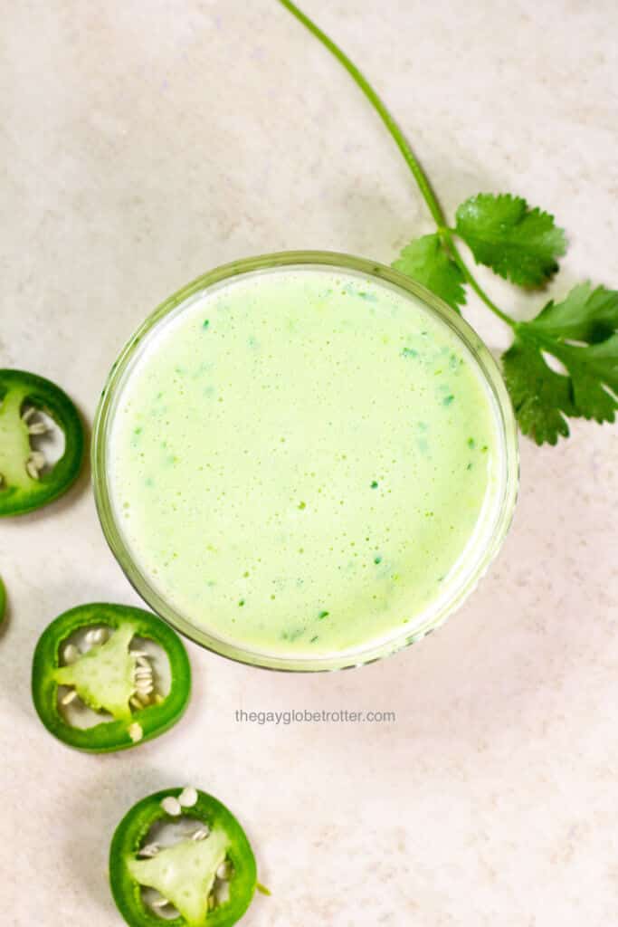 An overhead shot of a jar of Peruvian green sauce with cilantro and jalapenos next to it.