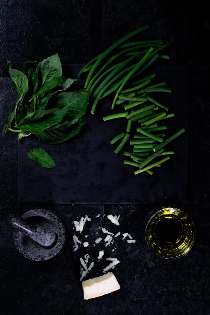 A working surface with ingredients for garlic scape pesto like basil and garlic scapes.