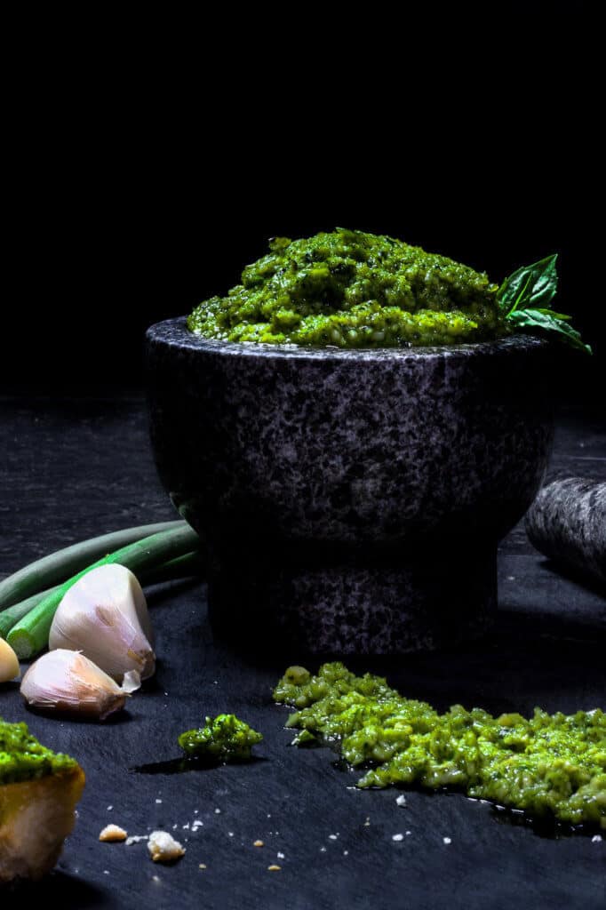 A bowl of garlic sc ape pesto with additional pesto in front of it.