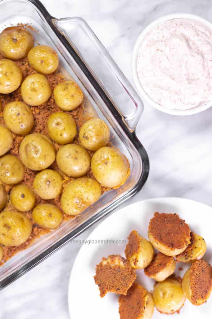 A dish of parmesan roasted potatoes fresh from the oven next to a plate and some dip.