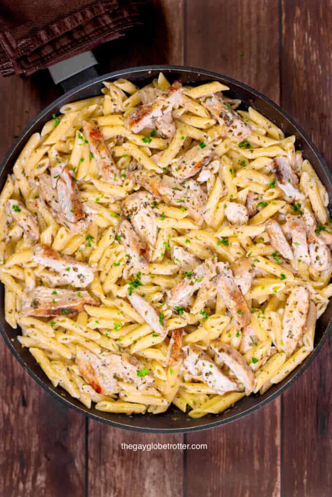 A pan full of creamy pesto pasta and chicken topped with fresh parsley.