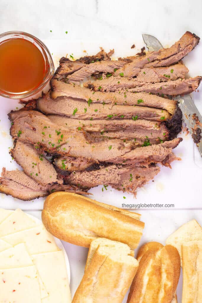 Sliced beef brisket on a cutting board with baguettes for french dip.