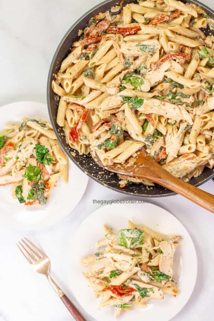 Tuscan chicken pasta being served from a pan to two serving plates.