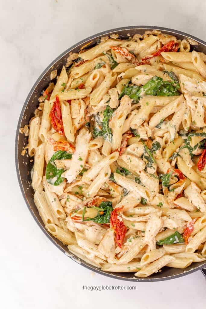 An overhead shot of a pan of tuscan chicken pasta with spinach, sun dried tomatoes, and chicken.