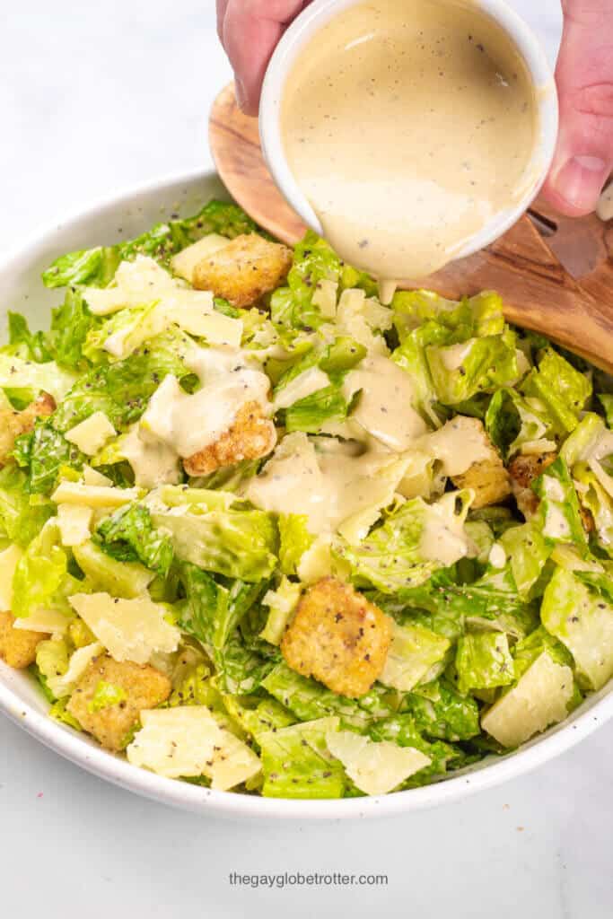 Caesar salad dressing being poured over caesar salad.