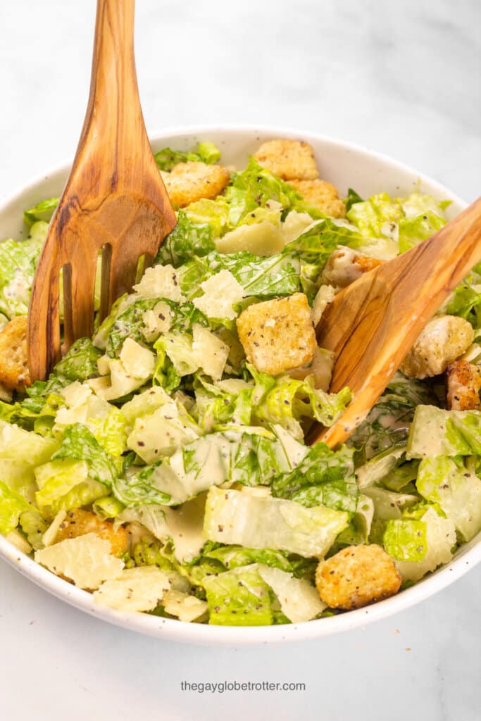 A caesar salad being tossed in a serving bowl with parmesan cheese and croutons.