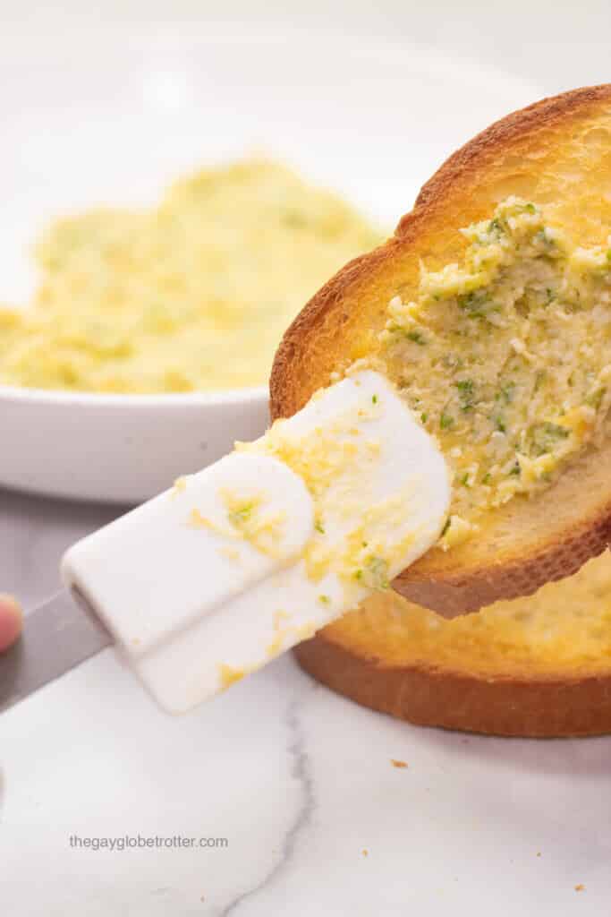 Roasted garlic butter being smeared on a slice of toasted bread.