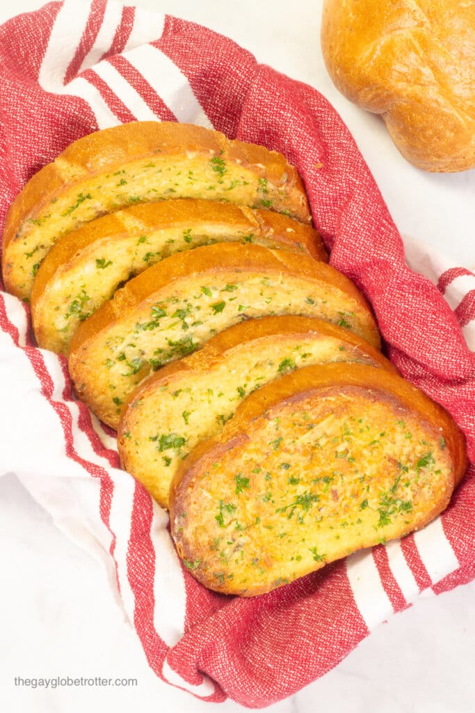 A basked of roasted garlic bread with a red tea towel in it.