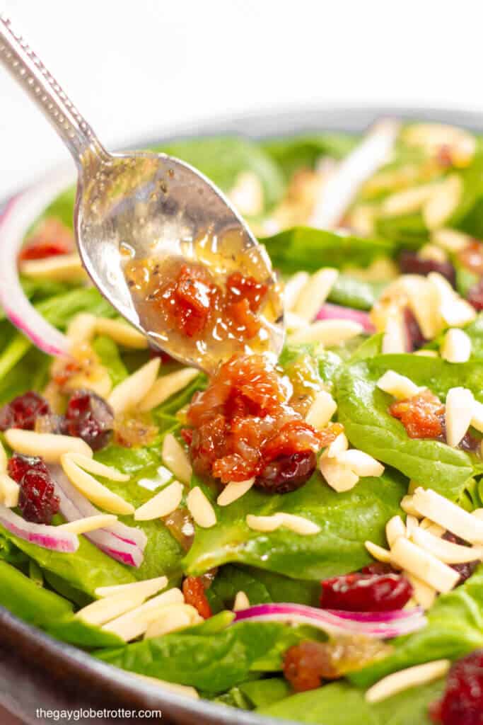 A spoon adding warm bacon dressing to spinach cranberry salad.