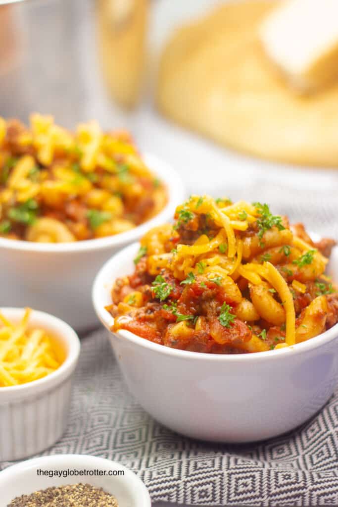 Two bowls full of american goulash topped with cheddar cheese and parsley.