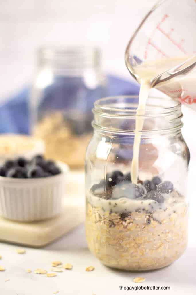 Almond milk being poured into a jar with oats, chia seeds, and blueberries.