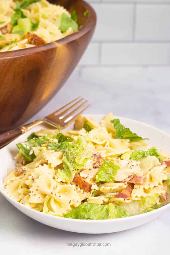 A white bowl full of chicken caesar pasta salad with a fork. 