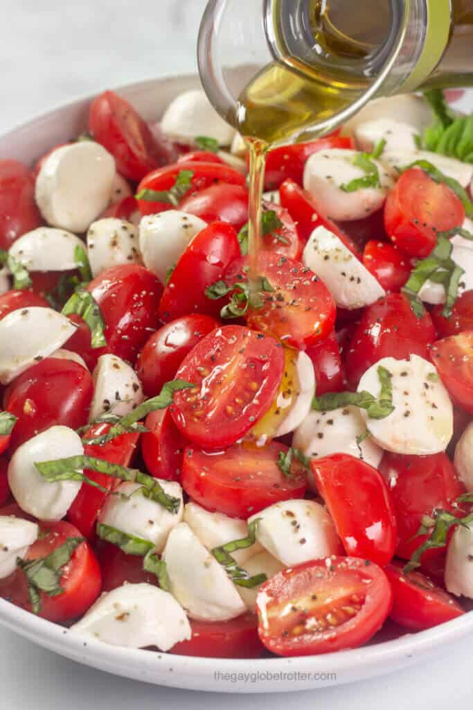 Olive oil being drizzled on cherry tomato caprese salad.