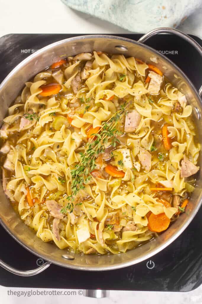 A pot of turkey noodle soup garnished with thyme.