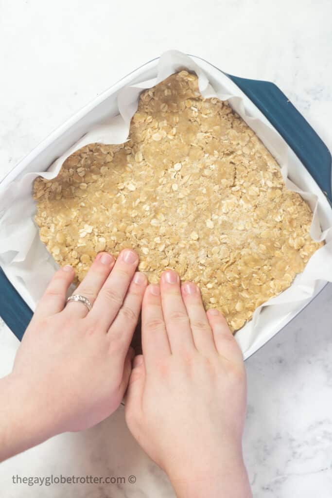 Oatmeal layer being pressed into a baking dish.