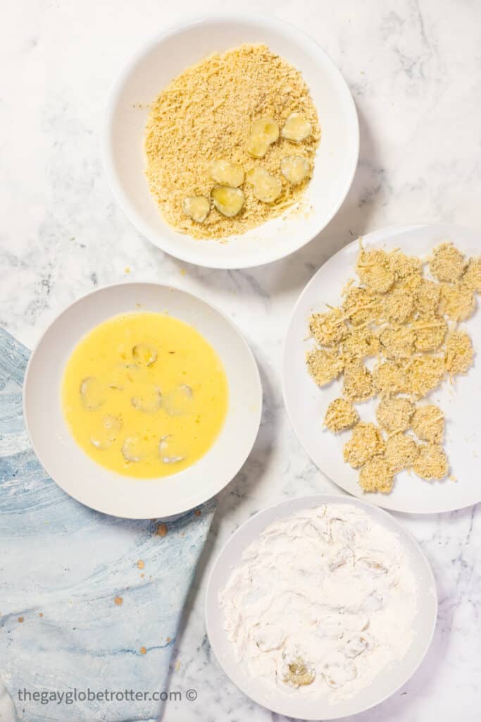 Pickles being breaded with egg wash, flour, and breadcrumbs.