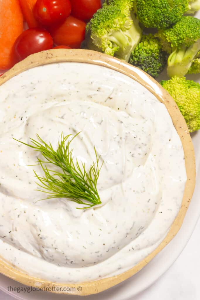 Fresh veggies next to a big bowl of dill dip garnished with fresh dill.