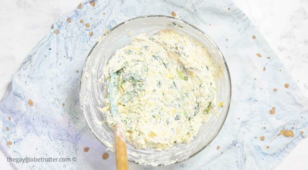 Spinach and artichokes being mixed into cream cheese.