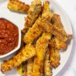 Air fryer zucchini fries on a plate next to marinara sauce.