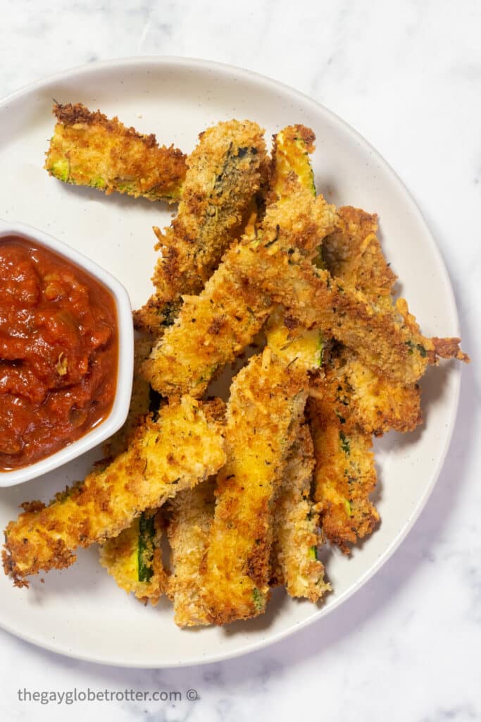 Air fryer zucchini fries on a plate next to marinara sauce.