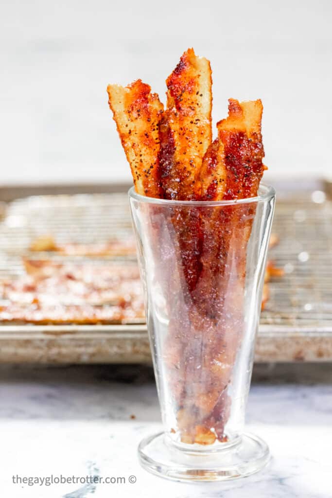 A cup of candied bacon next to a baking sheeet.