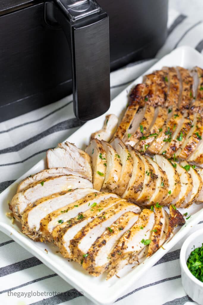 Sliced chicken breasts on a serving tray in front of an air fryer.