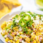 Mexican street corn on a serving plate garnished with cilantro with text overlay.