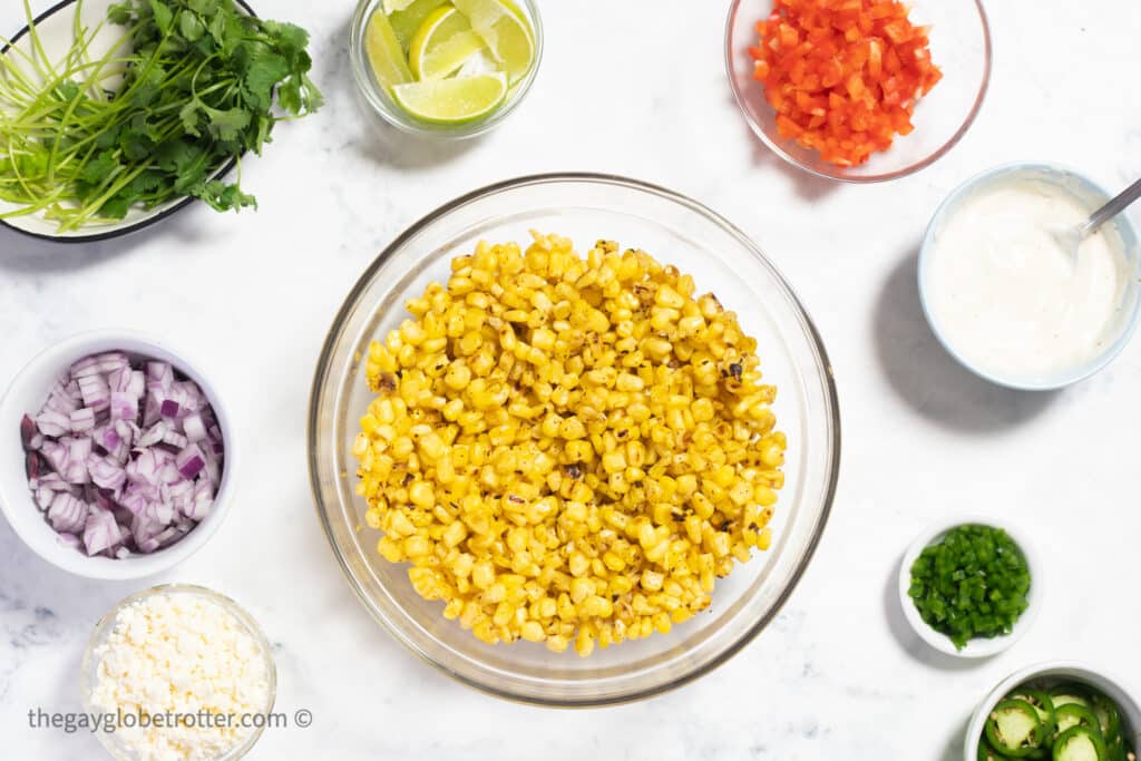 Mexican street corn dip ingredients like corn, red onions, cilantro, and red peppers in bowls.