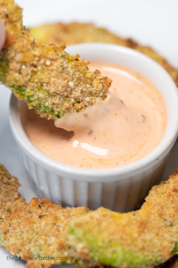 An avocado fry being dipped into sriracha ranch sauce.