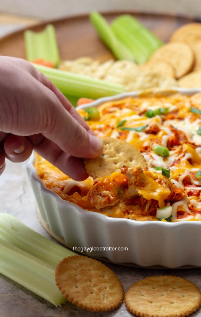 A Ritz cracker scooping buffalo chicken dip out of a serving bowl.