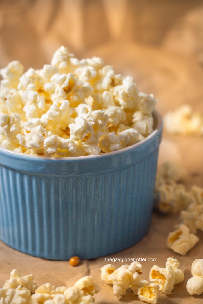 A blue bowl full of kettle corn with extra kettle corn around it.