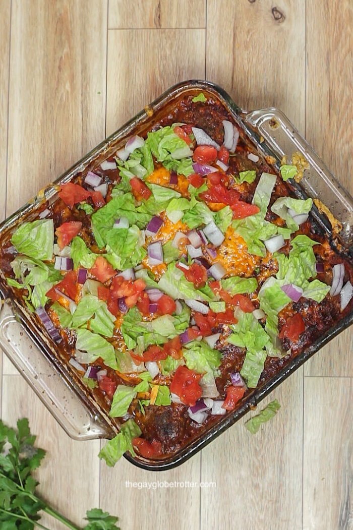 Taco meatball casserole in a baking dish topped with melted cheese, lettuce, tomatoes, and red onions.